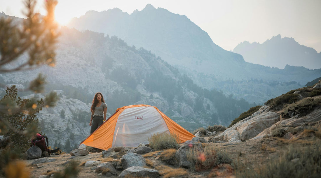 Women standing next to backpacking pack and tent with mountains all around. 